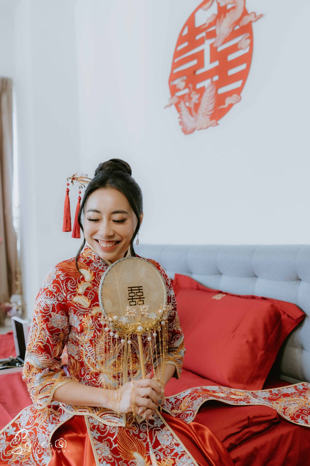 Queena holding a fan and smiling while looking away.